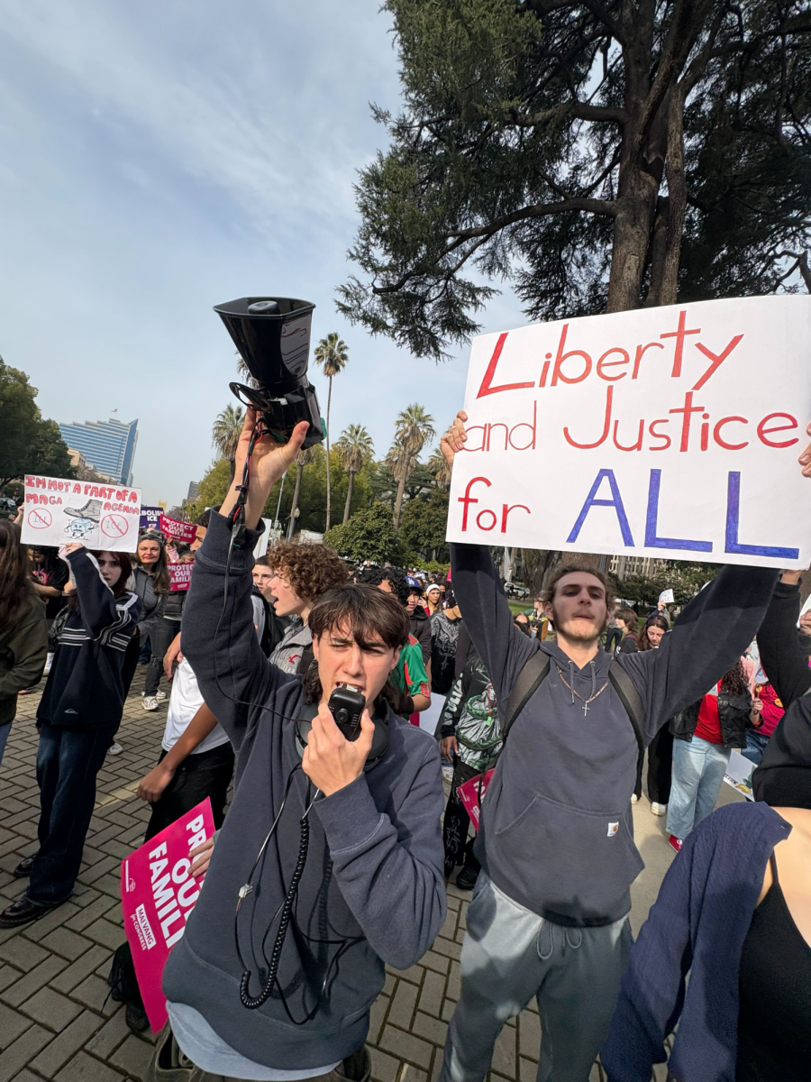 Vincent Rosales yells through a megaphone while another student holds up a protest sign on Friday Jan 30. The students were speaking at the event downtown.